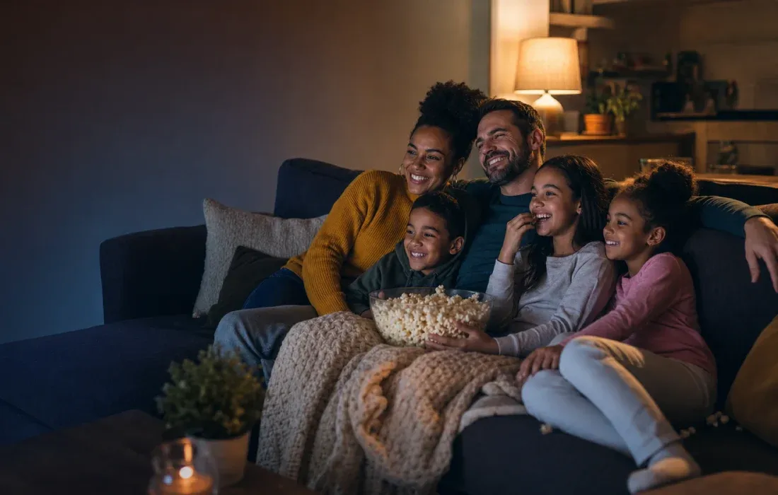 A foster family of two parents and three children snuggled together on the couch with popcorn for a cozy movie night